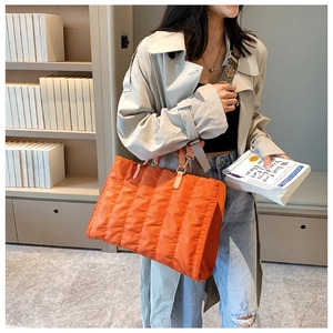 Orange quilted nylon tote bag worn by a model with a decorative patterned shoulder strap