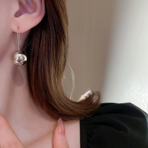 Close-up of minimalist silver metallic sphere earrings with long hook on model