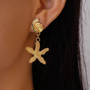 Close-up of golden starfish and seashell earrings with detailed textured metal finish