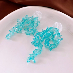 Detailed shot of irregular teal stone earrings on a white porcelain dish with fabric background