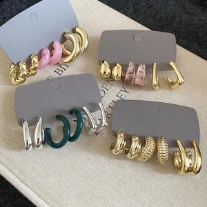 Macro detail of mixed acrylic and metal hoop earrings set on a textured beige background