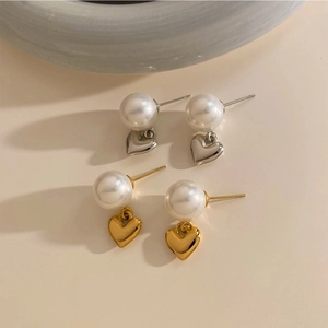 Elegante Herz-Ohrringe in Gold und Silber mit weißen Perlen auf warmem Hintergrund