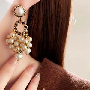 Macro view of vintage gold-tone round pearl tassel earrings shown on a female model