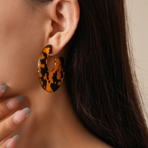 Detail of tortoiseshell acrylic C-shape hoop earrings on model for a modern elegant look
