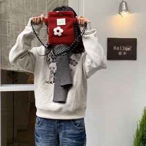 Detail of plush red crossbody bag with 3D white flower and woven shoulder strap