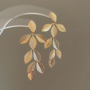 Detail of gold leaf tassel earrings with textured metal finish on a clear display stand