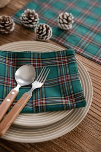 Close-up of red and green plaid placemat with wooden cutlery and ceramic dinnerware