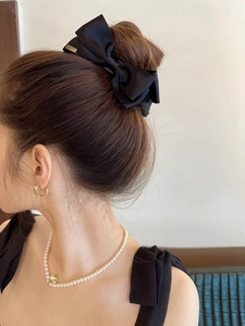 Detail of elegant black satin bow hair claw with gold metal tag and pearl necklace