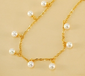 Detailed view of gold plated stainless steel anklet with pearls on soft beige fabric