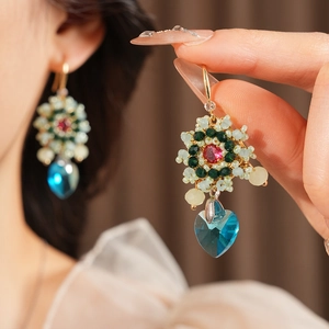 Dettaglio macro di orecchini vintage con cristallo a cuore blu e perline intrecciate