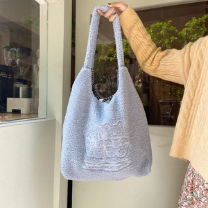 Detail of plush blue tote bag showing bear embroidery and black-and-white checkered lining