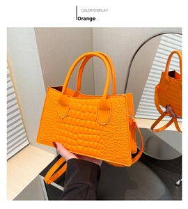 Detail of orange crocodile pattern handbag with dual handles and detachable shoulder strap