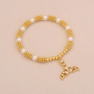Detailed shot of pearl and gold bead bracelet with crystal-studded fishtail charm