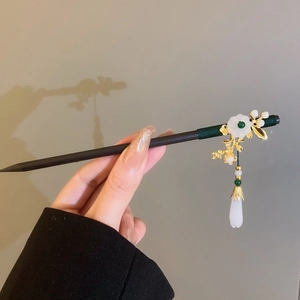 Detailed close-up of a vintage black wooden hair pin with golden petals and white flower