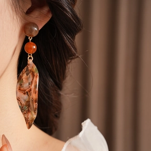 Close-up of amber acetate leaf earrings with beaded details worn by a model