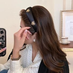 Detail of vintage black satin headband with gold heart accents on model with brown hair
