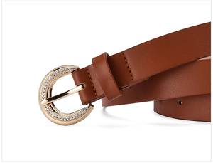 Close-up of golden horseshoe buckle with rhinestones on brown lychee grain leather belt