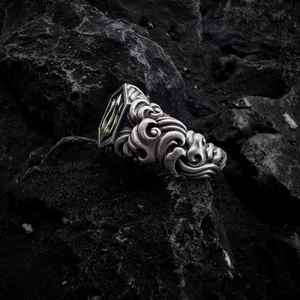 Detailed view of silver trident ring with wave textures on black volcanic rock base