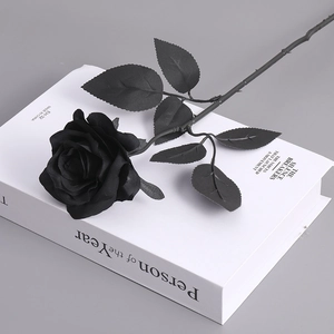 Gothic black artificial rose on white book background with realistic petal texture