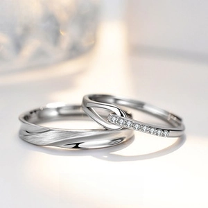 Close-up of interlocking S999 silver couple rings with brushed finish and inlaid stones