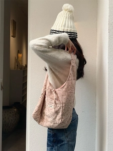 Pink floral corduroy tote bag with front pocket shown on shoulder in a minimalist room