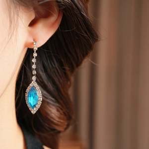 Close-up of model wearing long blue teardrop gemstone earrings with rhinestone tassels