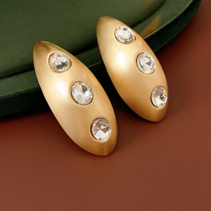 Macro shot of gold oval brushed stud earrings with three inlaid sparkling zircons