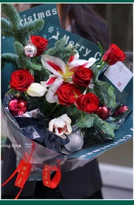 Close-up of Christmas bouquet with red roses, lilies, and Merry Christmas gold-edged ribbon