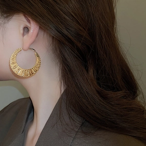 Detailed view of large gold twisted hoop earrings with ribbed texture on a model