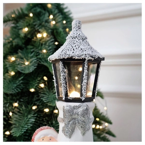 Close-up of ceramic Christmas lighthouse lamp with snow texture and silver glitter bow