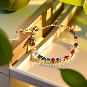 Detail of adjustable gold bracelet with colorful gems and a heart pendant in warm light