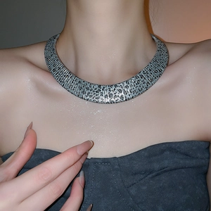 Detail of silver textured metal collar necklace showing intricate embossed pattern on model