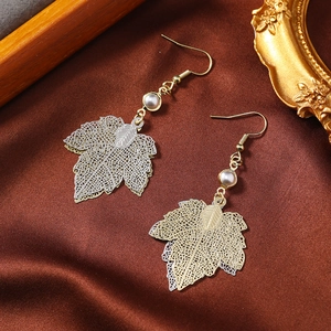 Golden and silver hollow maple leaf earrings with pearls on brown satin fabric