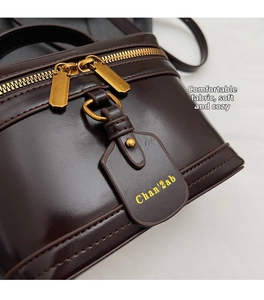 Detail of dark brown box bag with shiny leather texture and gold double zipper