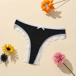Détail d'un string noir côtelé avec dentelle blanche et nœud sur fond floral beige