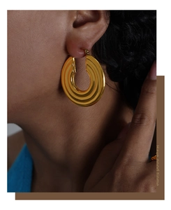 Detail of gold-plated geometric hoop earrings with unique wave texture on a model