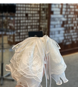 Détail d'une pince à cheveux en dentelle blanche avec couches d'organza et pompons perles