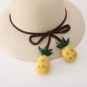 Détail d'un chapeau de paille beige avec nœud marron et mignons pendentifs ananas