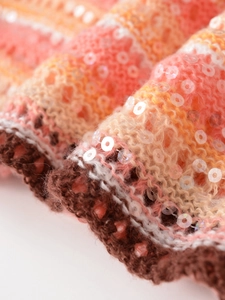 Nahaufnahme von Strickstoff mit Pailletten in orange, gelb und braun gestreiftem Muster