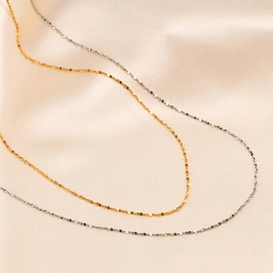 Close-up of gold and silver shimmering thin titanium steel chains on soft silk fabric