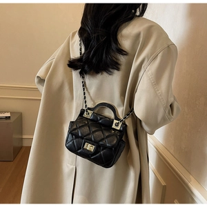 Detail of black quilted leather mini bag with gold chain strap on light trench coat