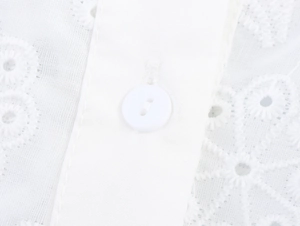 Detail of white button and hollow out lace embroidery texture on a French style top