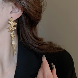 Close-up of golden butterfly earrings with flower tassels on a model side profile