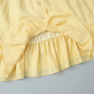 Detail of light yellow dress hem showing small buttons and ruffled pleat texture