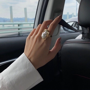 Close-up of irregular gold ring with baroque pearl worn against a city backdrop