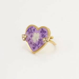 Golden heart ring with purple dried flowers and rhinestones on a white background