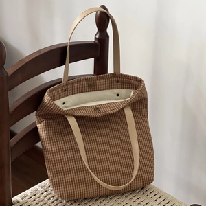 Detail of vintage brown plaid tote bag with leather handles on a wooden chair