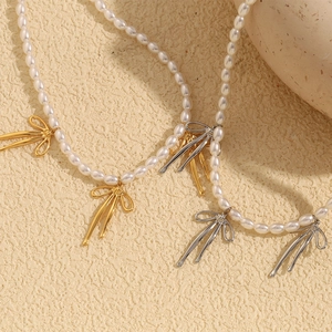 Détails des pendentifs nœuds dorés et argentés sur des colliers de perles blanches chics
