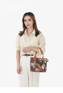 Detail of geometric patchwork tote bag with decorative scarf handle held by a model