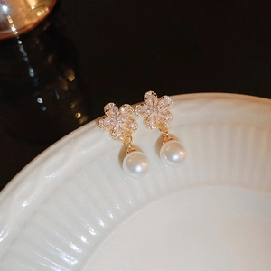 Macro detail of gold flower earrings with pavé diamonds and a white pearl drop